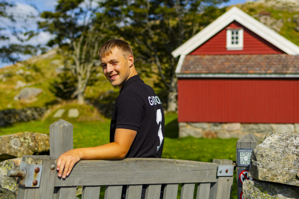 Museum worker outside the gate of the red summer house Knudaheio, which renowned author couple Arne and Hulda Garborg found their peace and quiet amidst the majestic hills looking out on Jæren and the sea in the distance